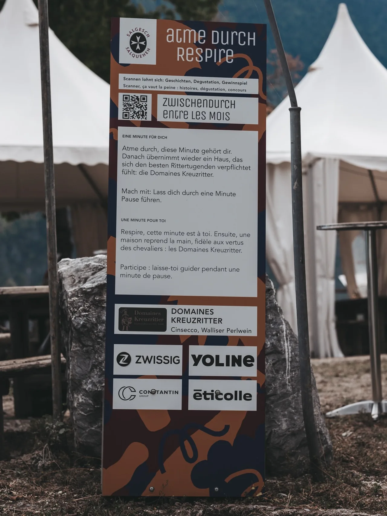 Eine Stele mit QR-Code und Text vor Festzelten.